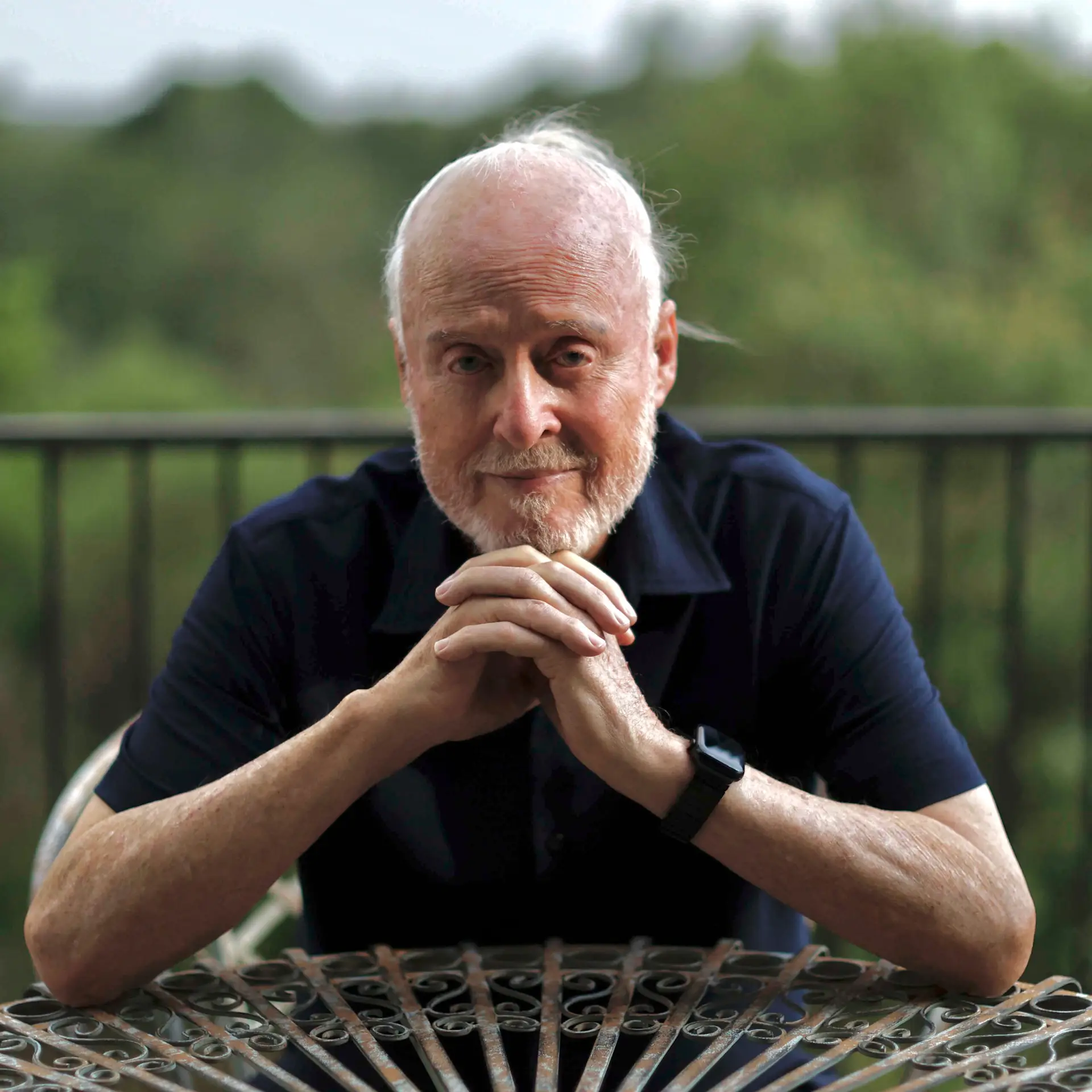 James M. Sweeney sitting at an iron table with his hands clasped and chin on his hands