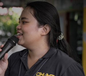 A young woman wearing an OUR Resue shirt speaks with a microphone. Serving others is one way of expressing gratitude. 